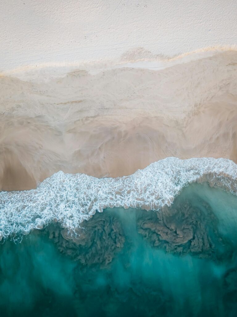 A stunning aerial view showcasing a sandy beach meeting the turquoise ocean waves. Perfect for travel and nature themes.