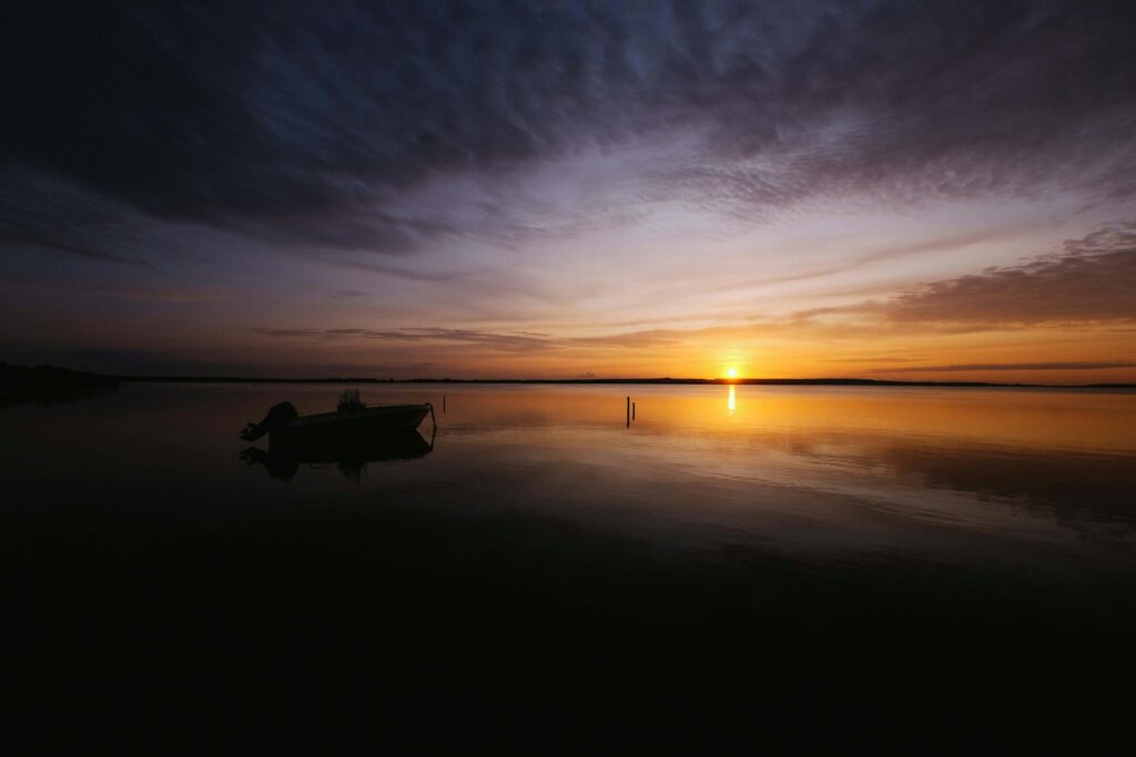 Calm sunset over a tranquil lake with boat silhouette, reflecting golden hues on calm water.